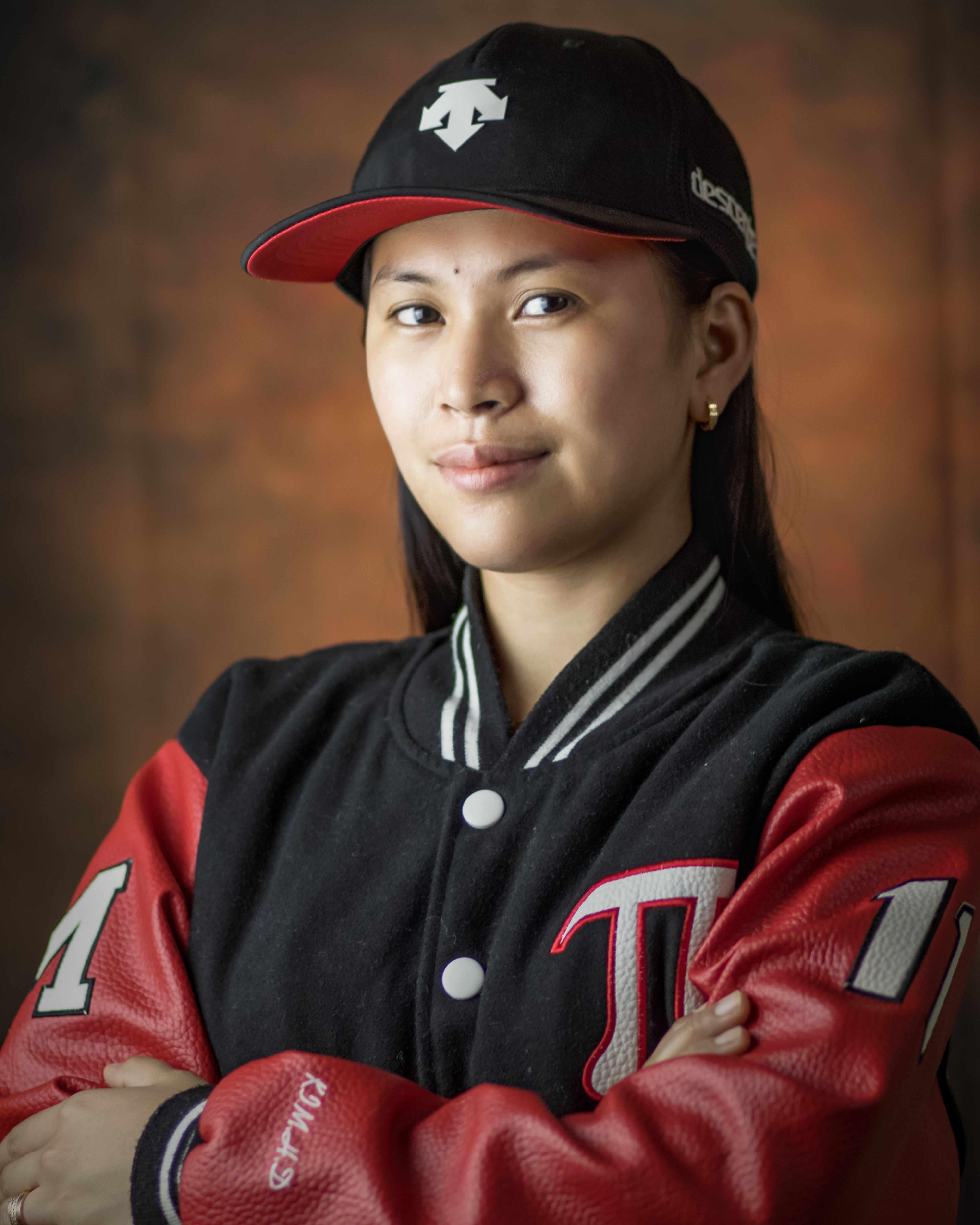 Portrait of a confident young woman wearing a varsity jacket and cap indoors.