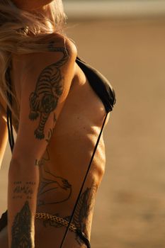 Woman with tattoos in a black bikini enjoying a sunny beach day. Side view.