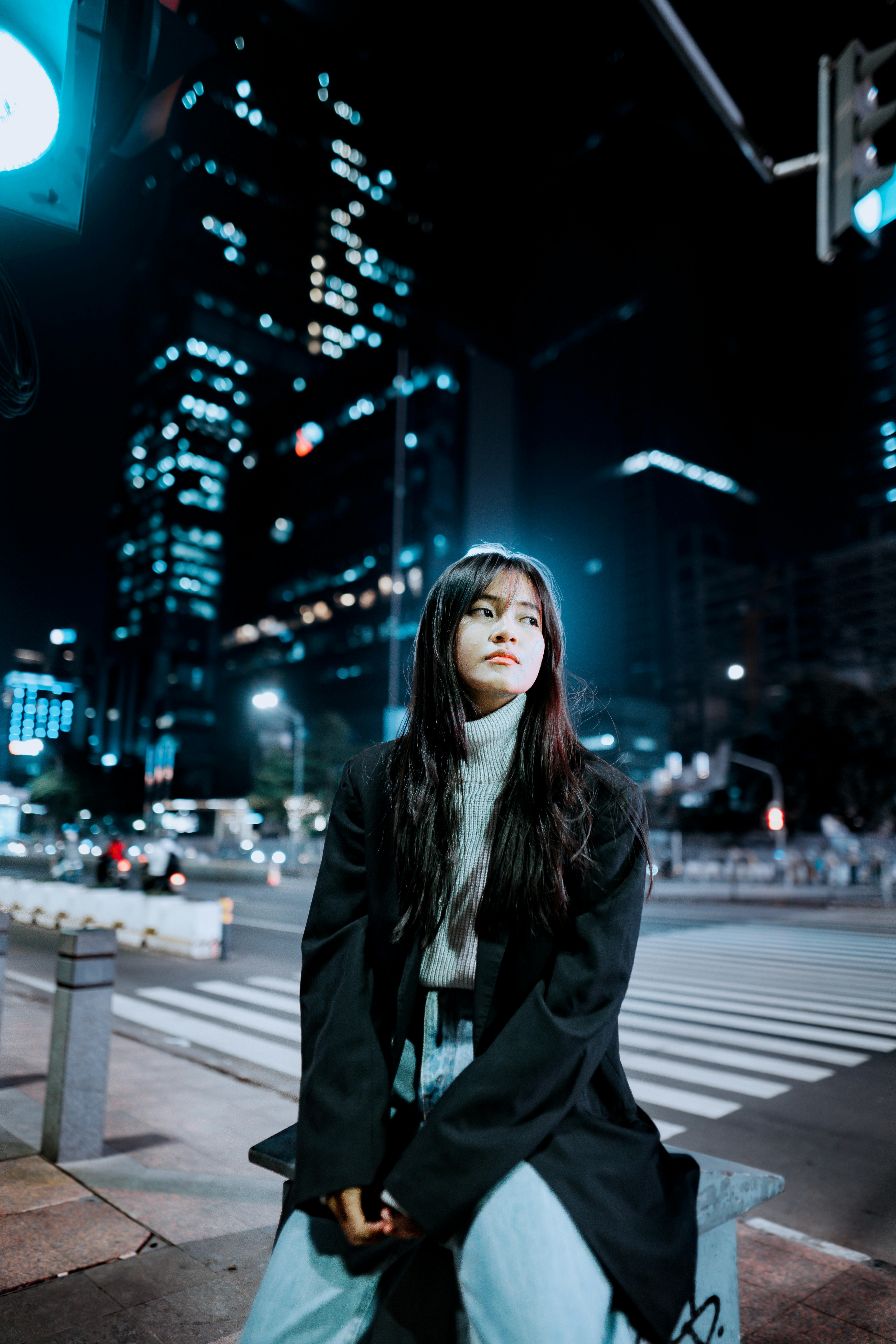 Portrait of a young woman sitting on a city bench in Jakarta's vibrant night scene.