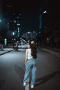 Woman in White Tank Top and Blue Denim Jeans Standing on Sidewalk during Night Time