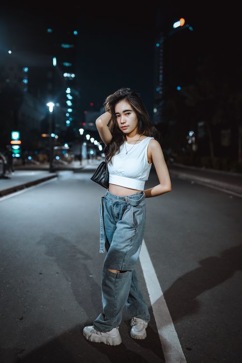 Free Stylish Asian woman in crop top and denim jeans posing on a city street at night. Stock Photo
