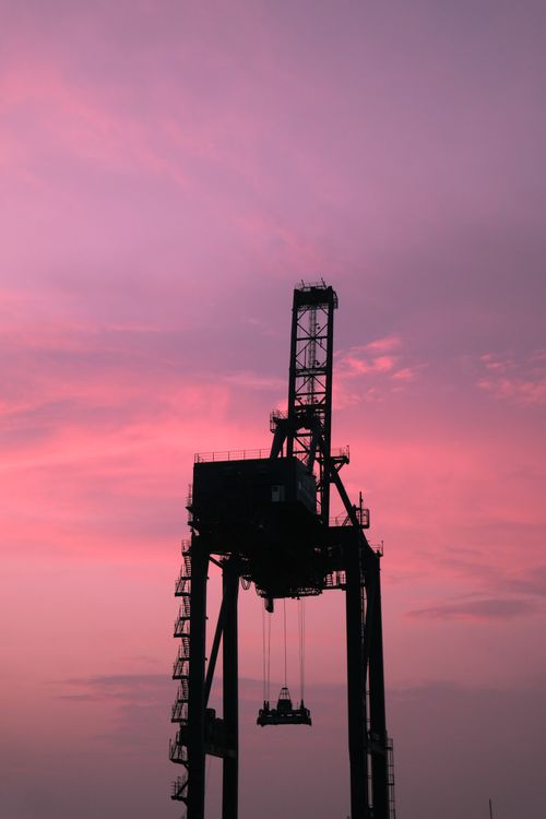 Free A large industrial crane silhouetted against a vivid pink sunset sky, capturing the essence of industry at dusk. Stock Photo