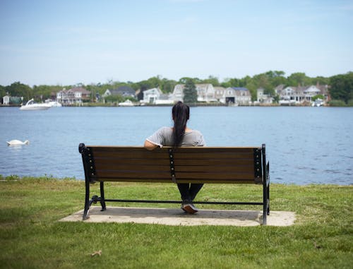 Woman Sitting on Brown Wooden Bench Facing Body of Water