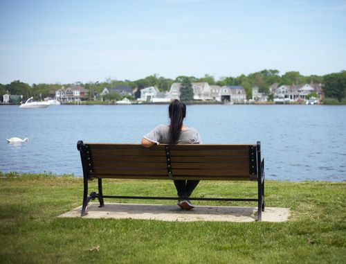 Free Woman enjoying a serene view of the lake from a bench in Great River, NY. Stock Photo