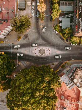 Aerial shot of a city intersection with cars and greenery, showcasing urban traffic flow.