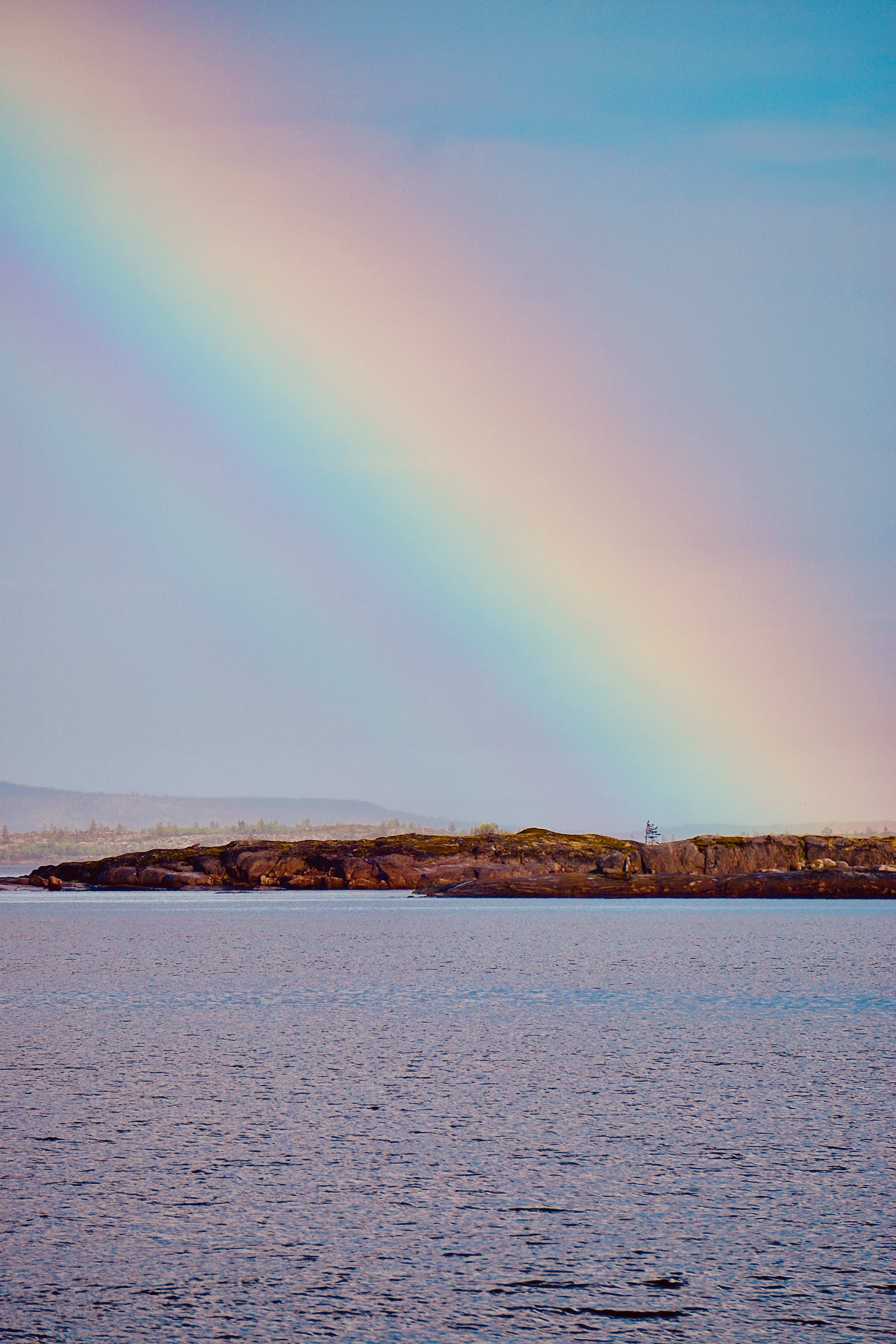A stunning rainbow arches over a tranquil coastal scene with calm sea and rocky horizon.