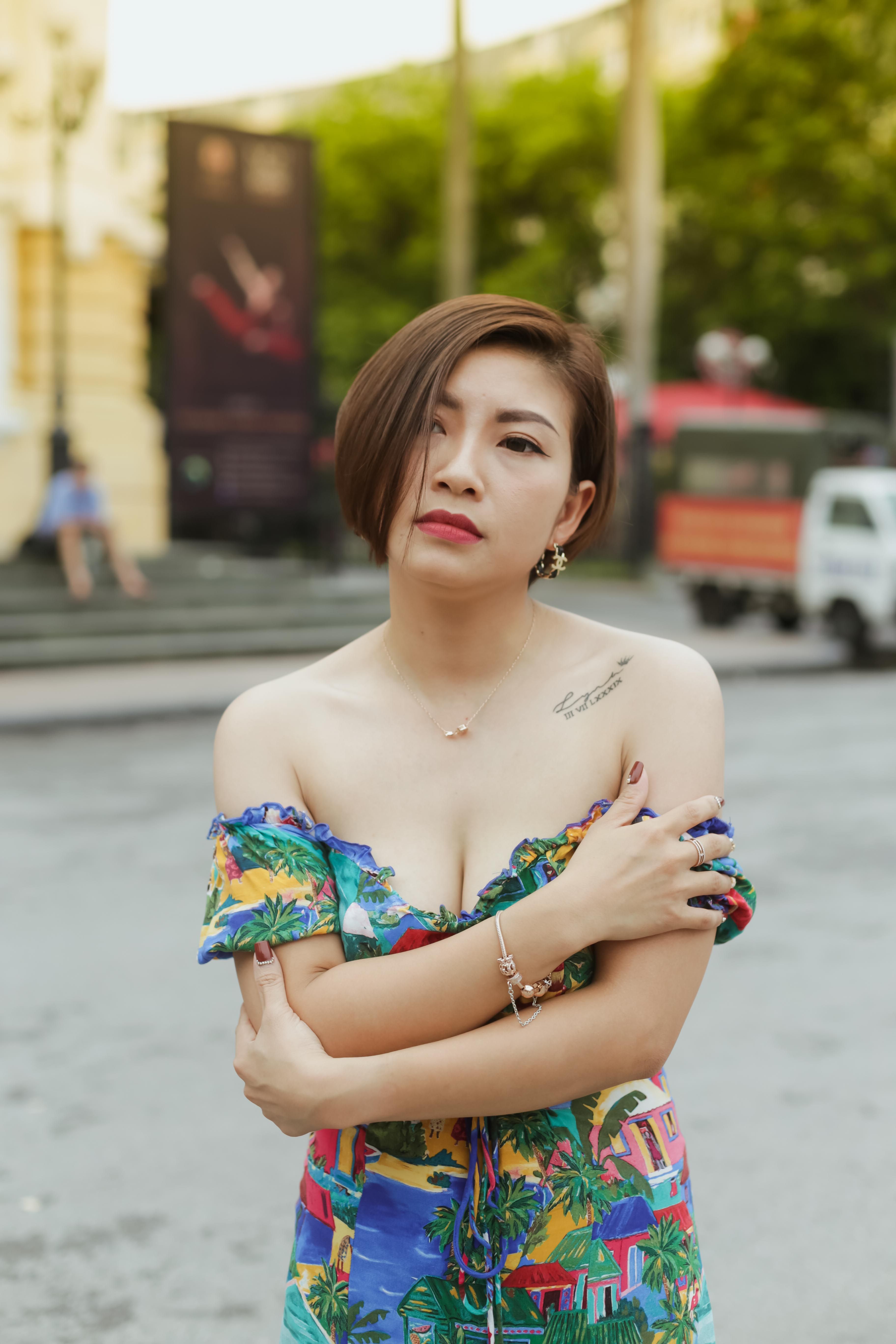 A stylish woman standing on a street wearing a colorful off-shoulder dress, showcasing a modern tattoo.