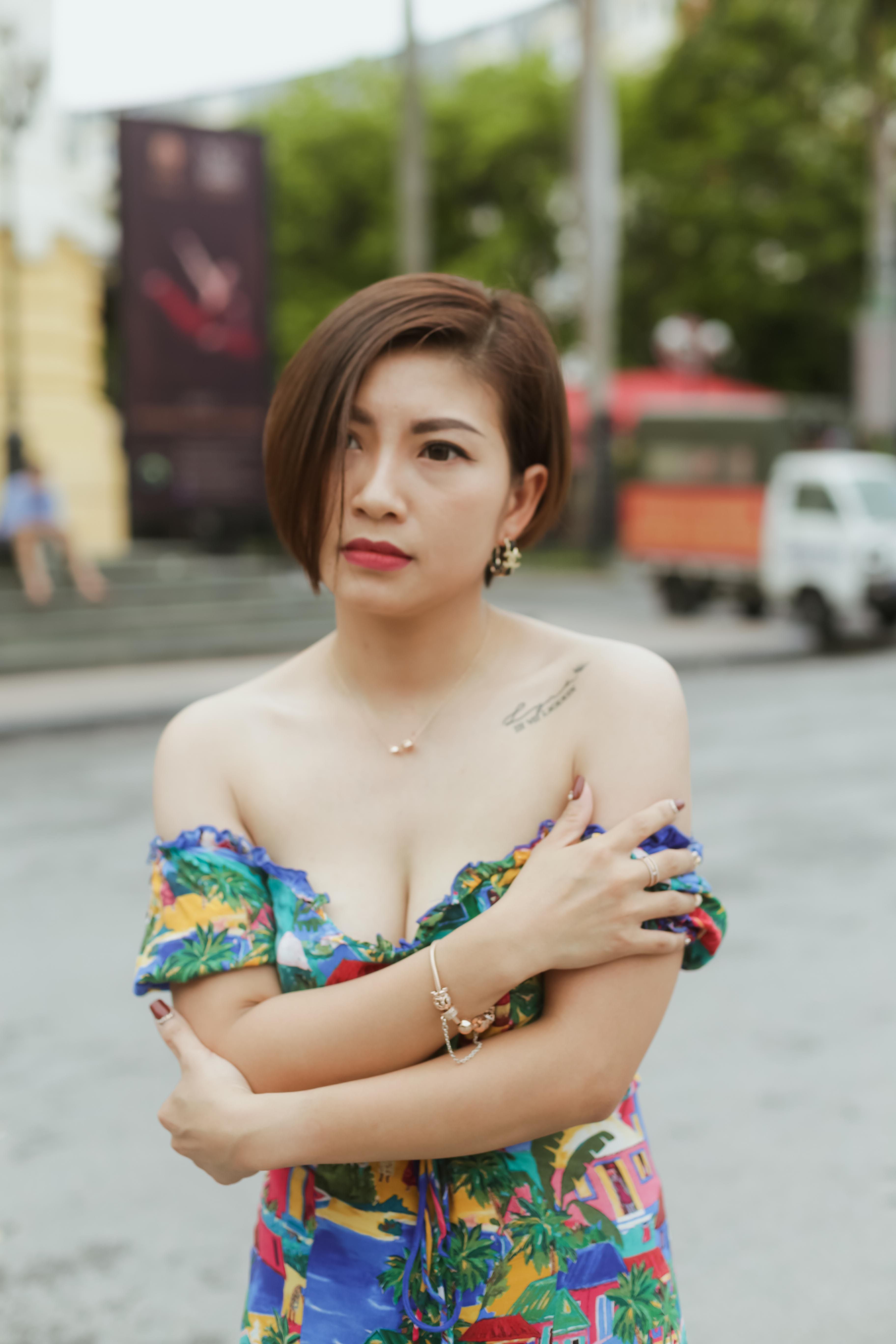 Portrait of a young woman in an off-shoulder dress on a lively street with tattoo and stylish look.