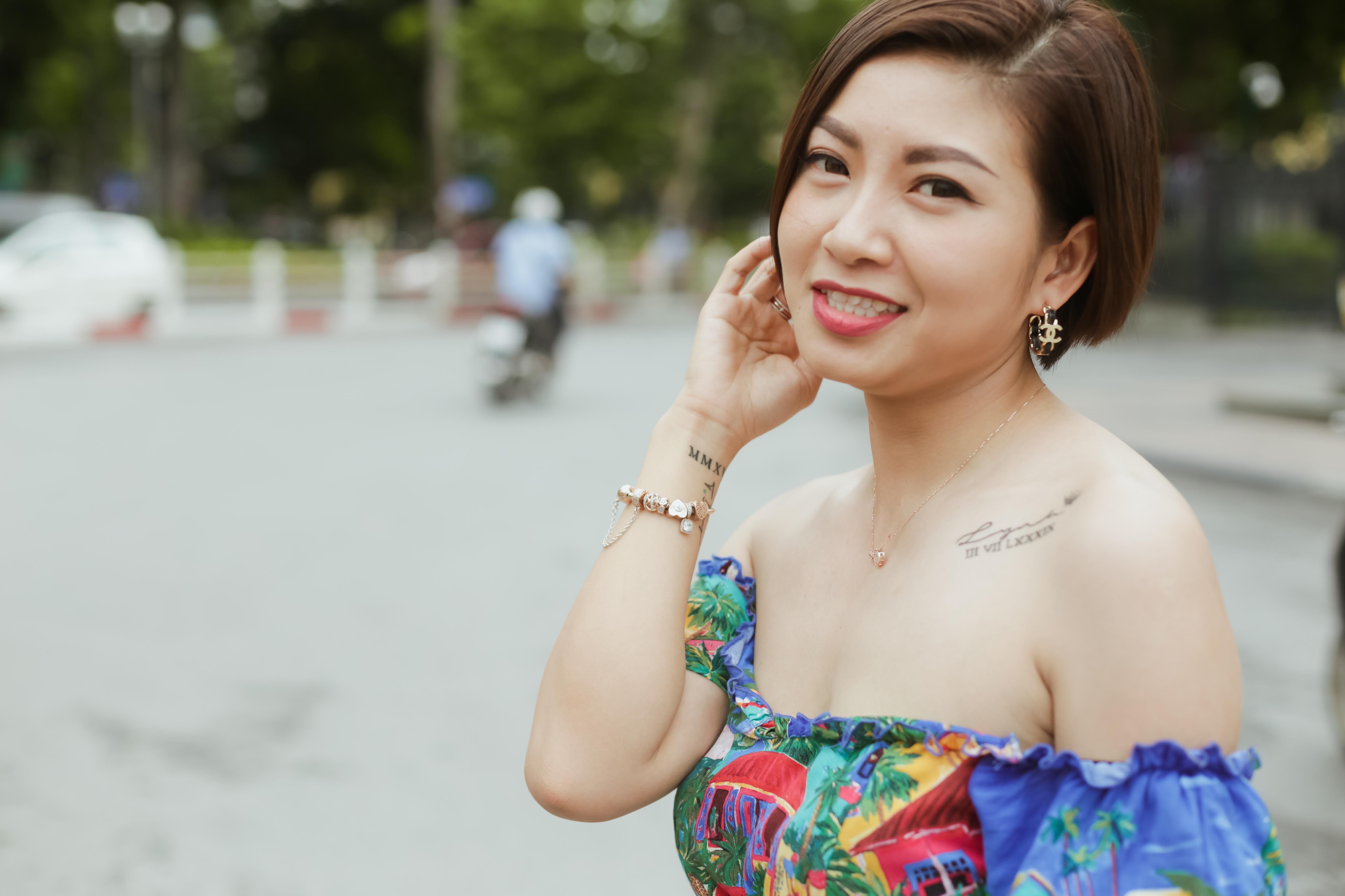 Smiling woman in a colorful dress with tattoos posing on a street.