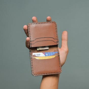 A hand holding a leather wallet containing various cards and cash.