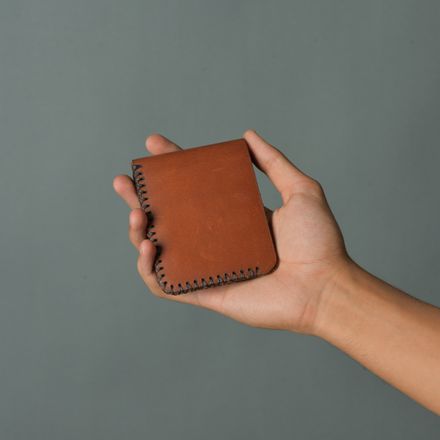 Hand holding a stitched brown leather bifold wallet — photo by Candy Flipping on Pexels