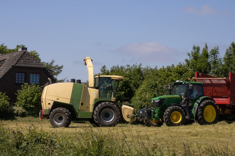 A Krone Big X Chopper And John Deere Tractor On A Grass Field