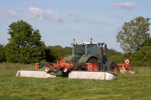Free A powerful modern tractor mowing fields in a lush, sunny countryside, showcasing agricultural machinery at work. Stock Photo