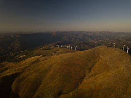 Вид с воздуха на белые турбины на холмах, покрытых зеленой травой