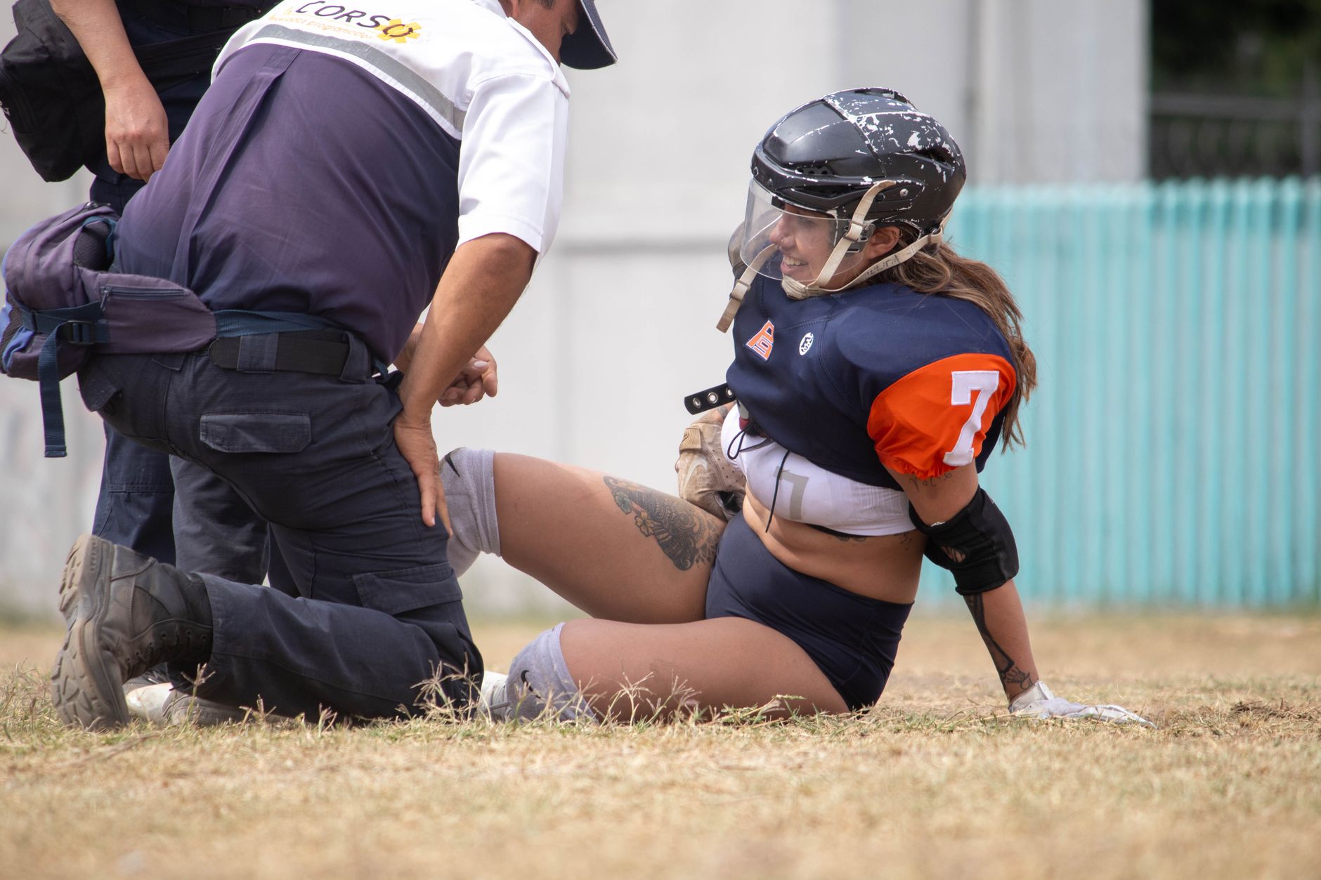A female rugby player receives assistance from a medic on the field after an injury.