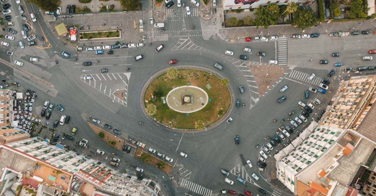 Bird's eye view of a busy traffic circle in an urban setting with cars and buildings.