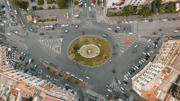 Bird's eye view of a busy traffic circle in an urban setting with cars and buildings.