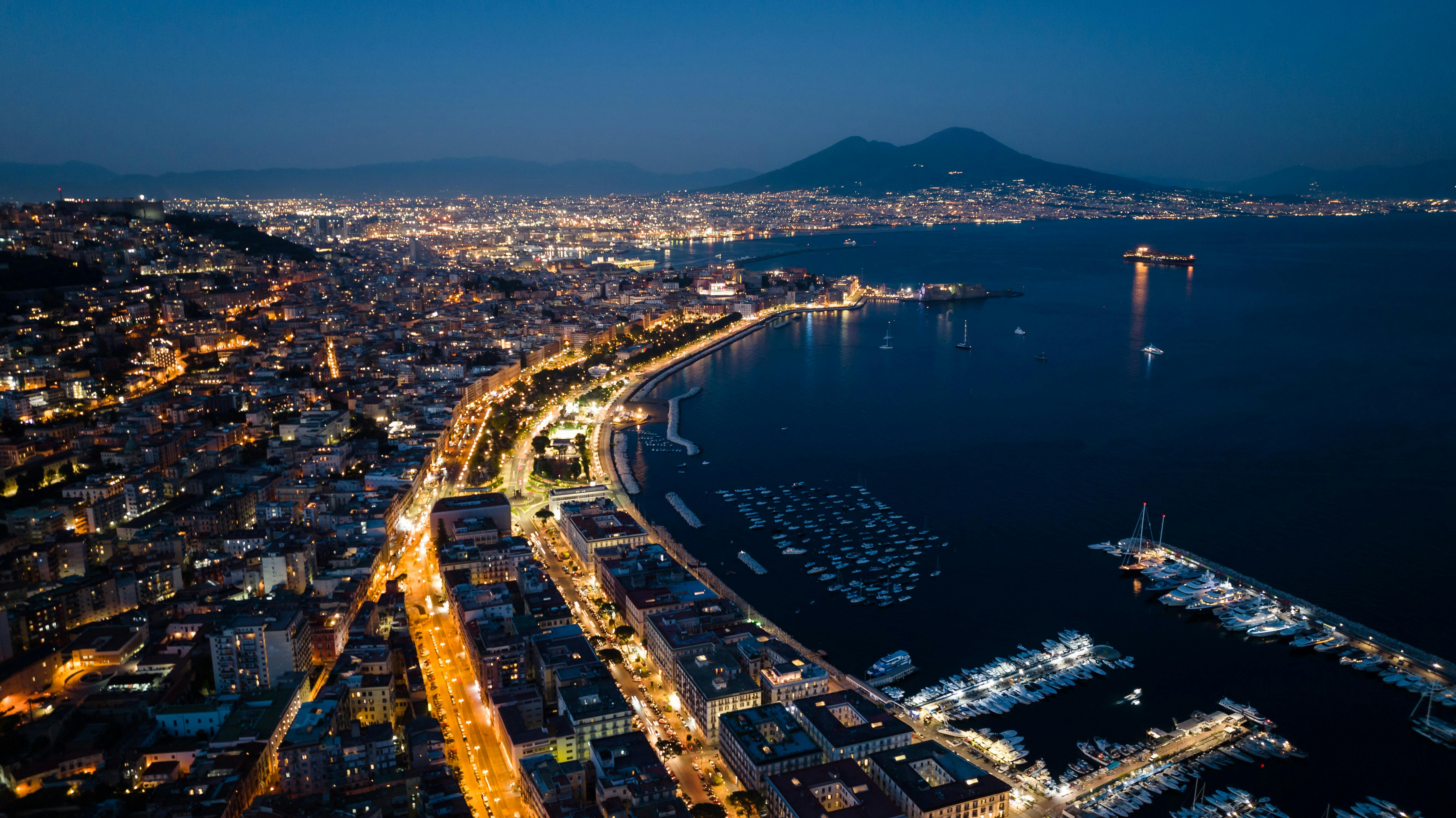 Stunning aerial view of Naples cityscape and harbor, illuminated at night with Mount Vesuvius in the background.