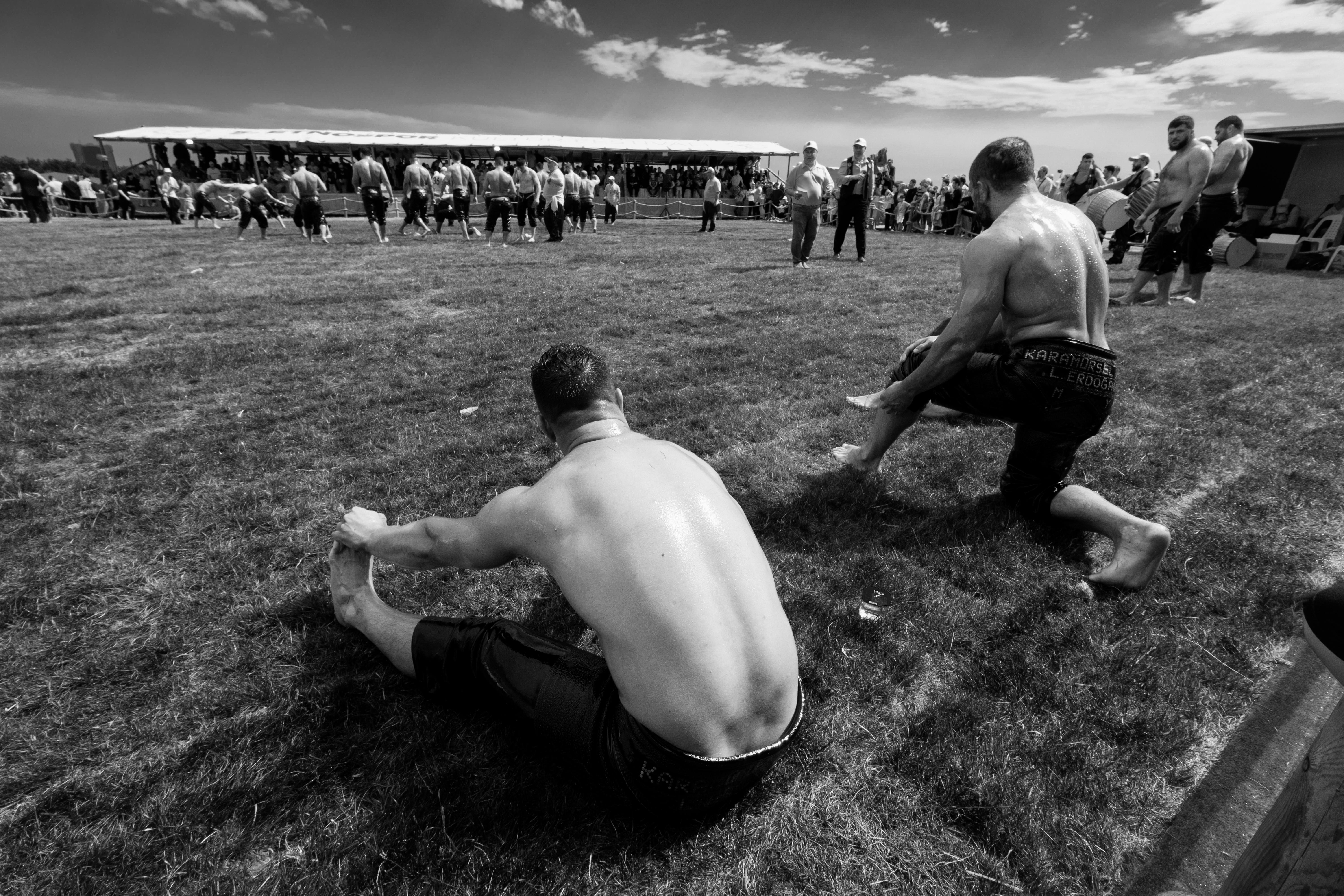 A group of shirtless men stretching on a grass field during a sports event, captured in black and white.