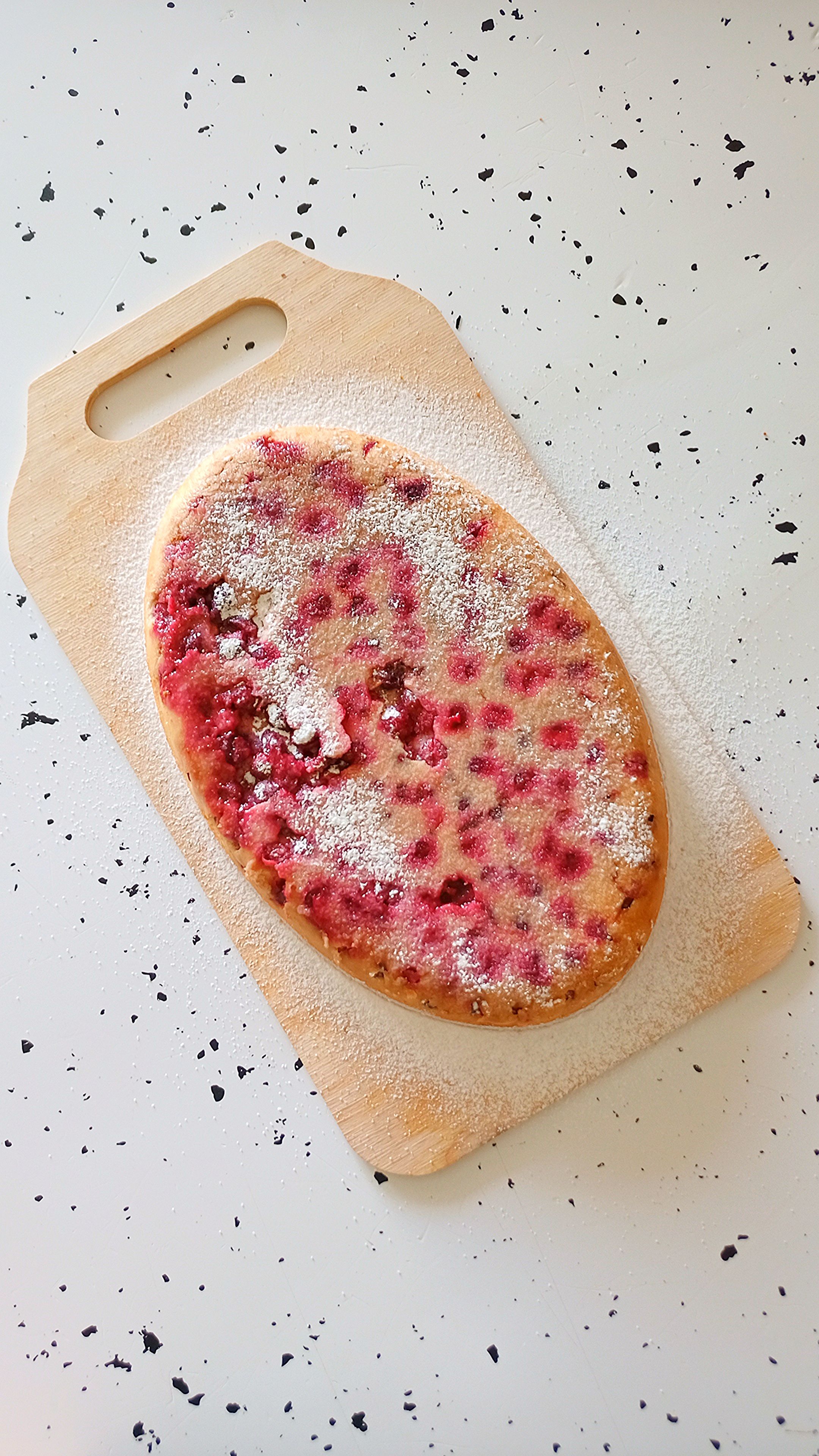 Top view of a rustic berry tart with powdered sugar on a wooden board.