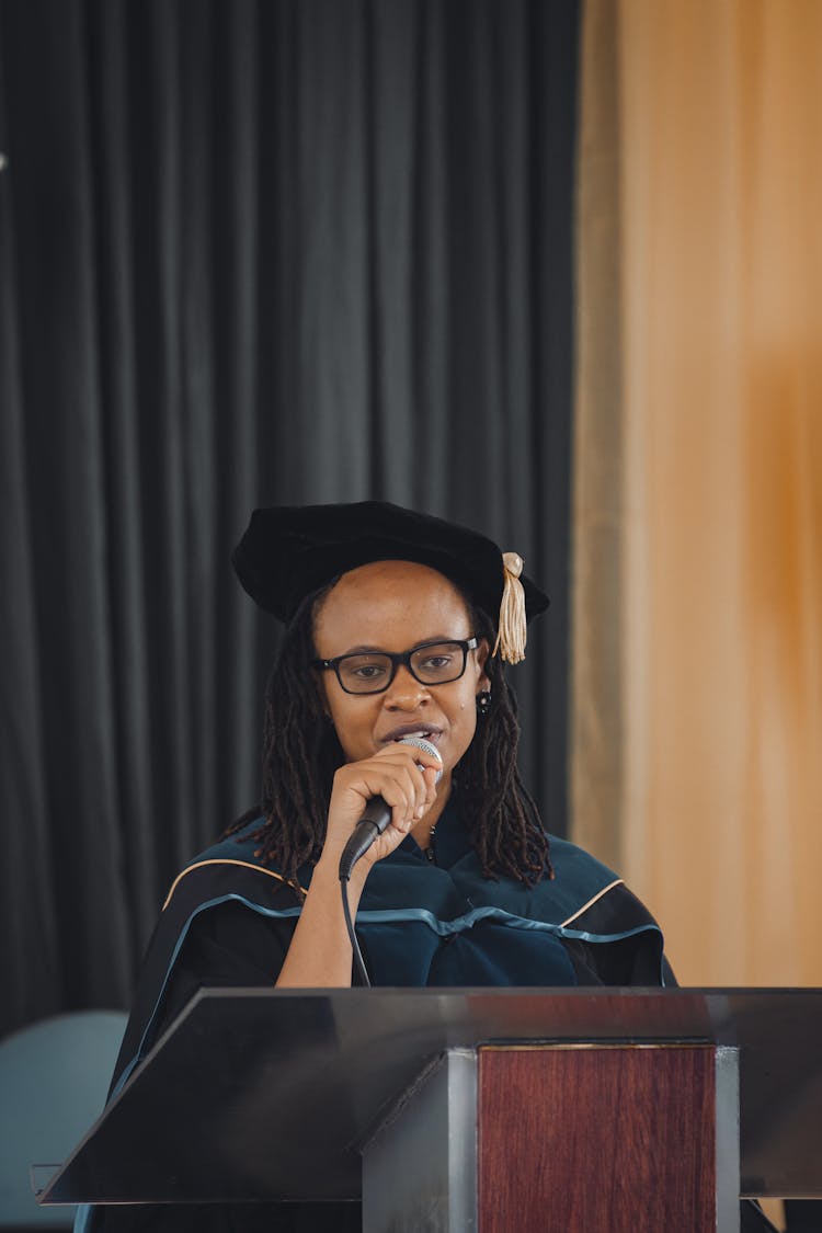 Woman In A Graduation Gown Giving A Speech