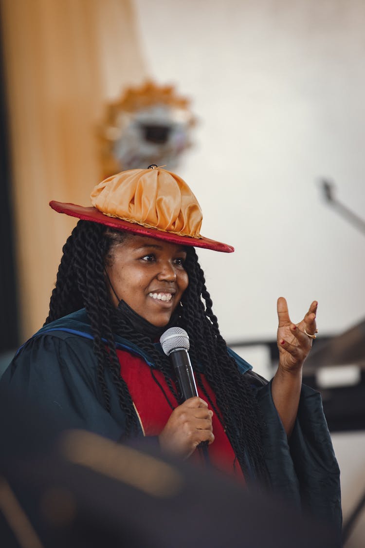 Woman In A Graduation Gown Giving A Speech And Smiling 