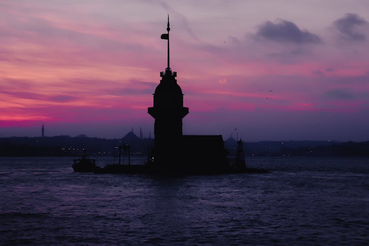 Silhouette Of Lighthouse On Water On Dramatic Sky Background