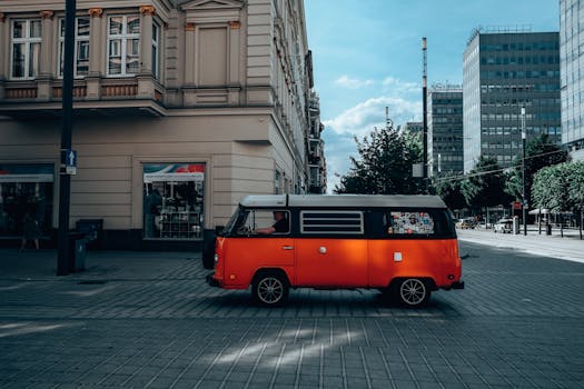 A vibrant orange vintage Volkswagen van on a sunny street in Poznan, showcasing classic architecture.