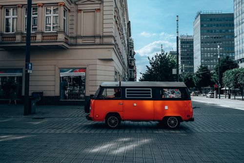Free A vibrant orange vintage Volkswagen van on a sunny street in Poznan, showcasing classic architecture. Stock Photo