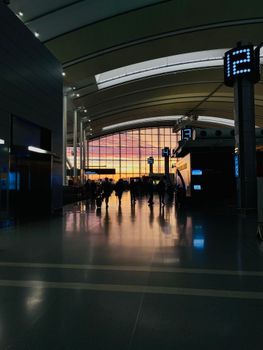 Silhouetted travelers in an airport terminal with vibrant sunset background.