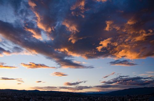 Free A stunning sunset sky with dramatic clouds over a silhouette cityscape. Stock Photo