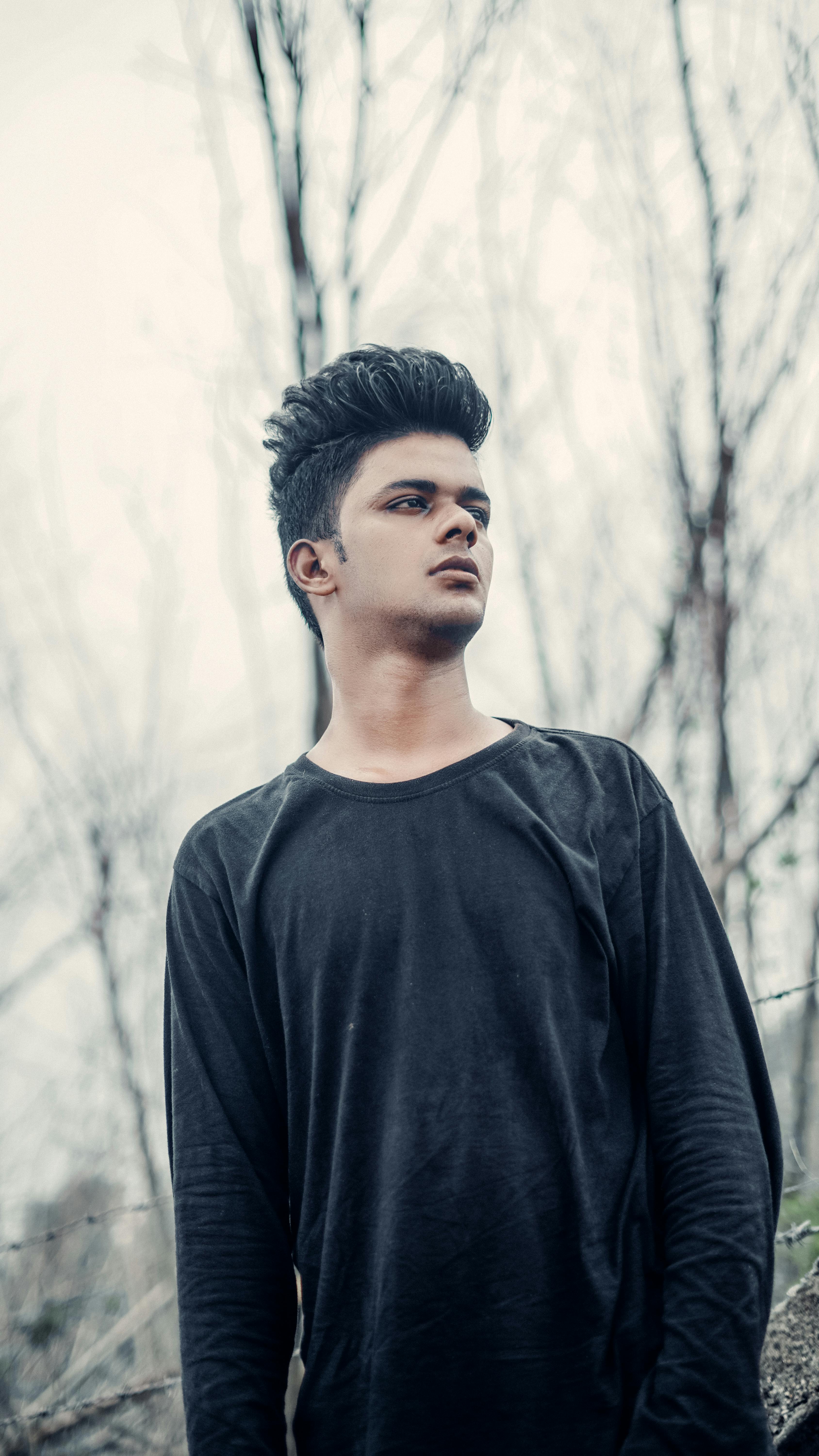 Portrait of a stylish young man wearing a black sweater, standing outdoors against a natural background.