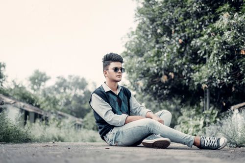Free Young man in sunglasses sitting on pavement surrounded by greenery on a sunny day. Stock Photo