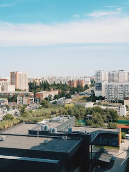 A sprawling modern city skyline featuring high-rise buildings, greenery, and blue skies.