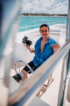Man in blue shirt relaxing on a yacht holding a camera, enjoying a sunny day at sea.