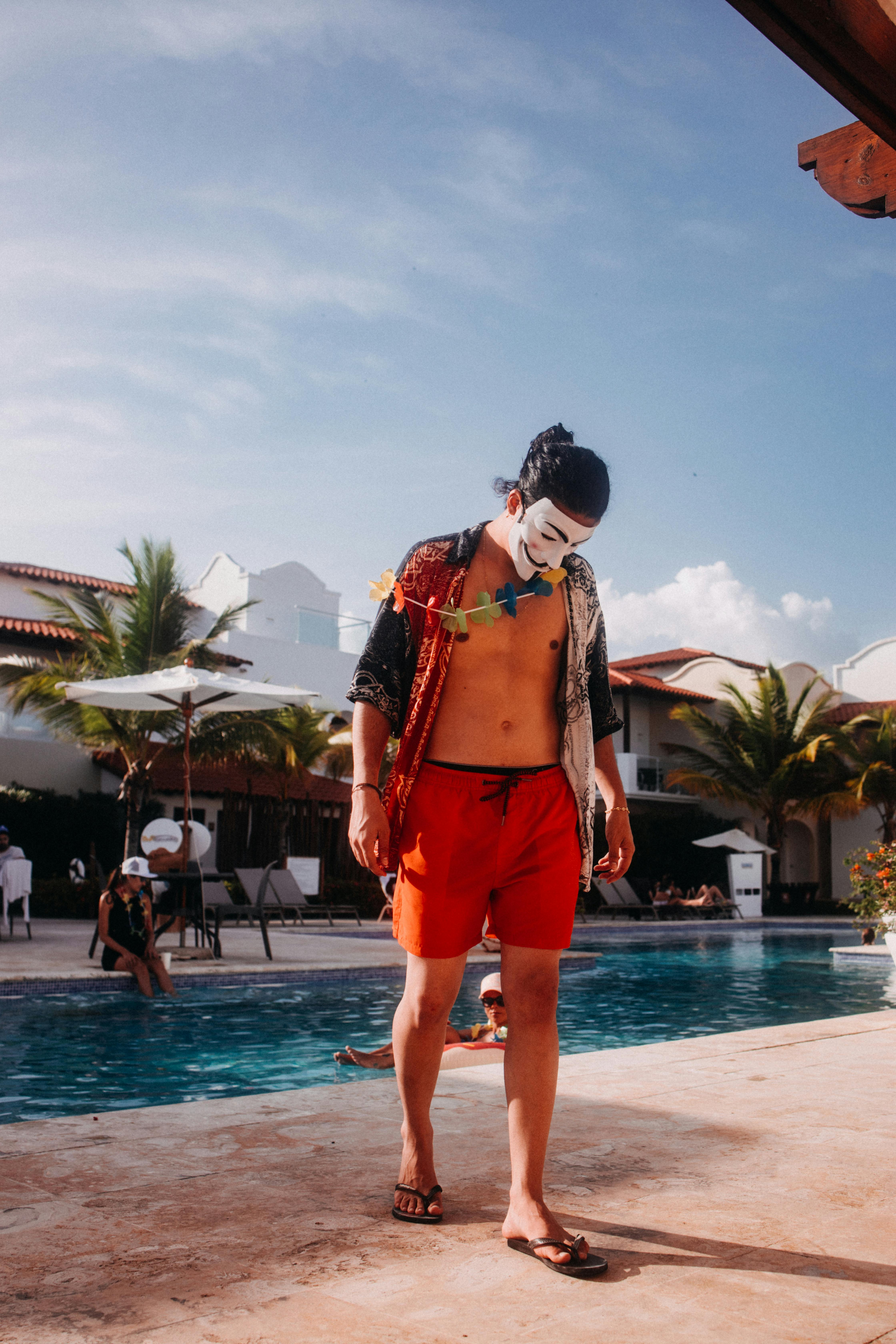 Free A man in a colorful mask strolling poolside at a tropical resort, showcasing a relaxed vacation vibe. Stock Photo