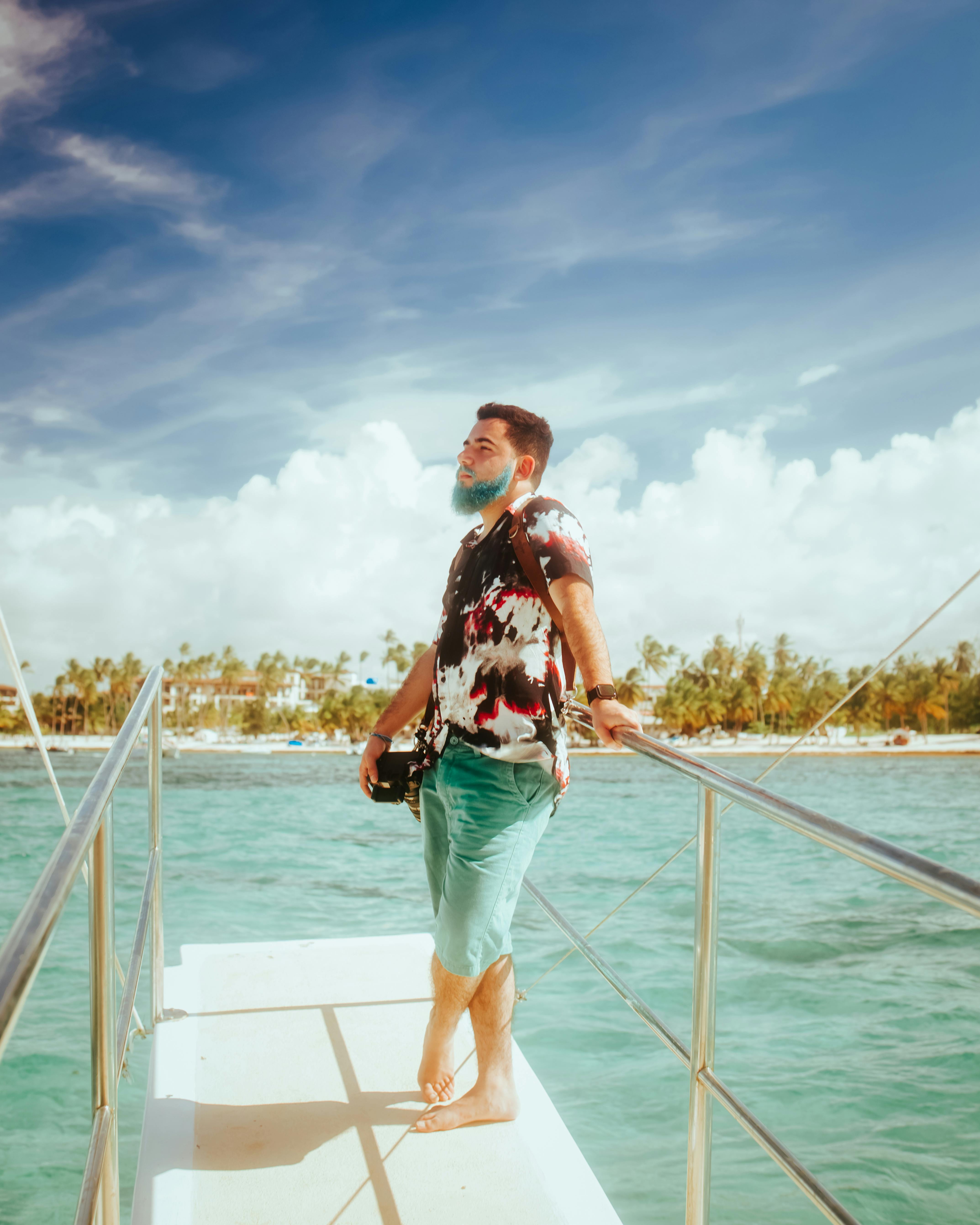 Man standing on a boat deck, enjoying a sunny ocean view with palm trees in the background.