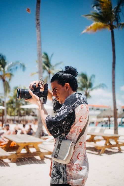 Free A man taking photographs on a sunny beach, showcasing leisure and travel vibes. Stock Photo