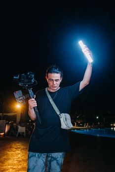 Man holding a camera rig and LED light at night, capturing a vibrant scene.