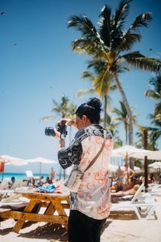 A photographer takes pictures on a sunny beach with palm trees and beach loungers.