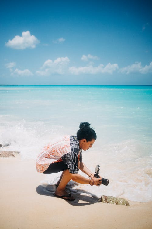 A Man Sitting on Seashore Holding a Camera