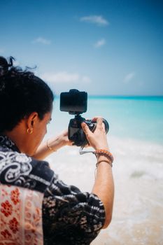 A photographer takes a picture of a vibrant beach scene with a digital camera by the sea.