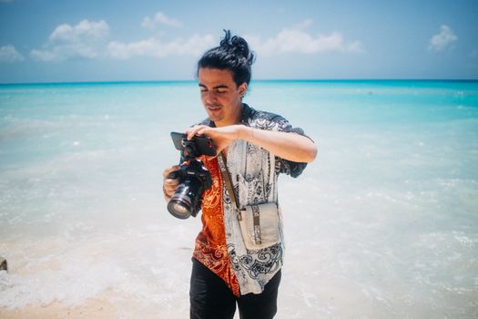 A photographer with a camera captures stunning ocean views on a sunny tropical beach.