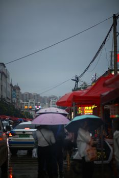 Crowded street with people under umbrellas during rain in urban setting.