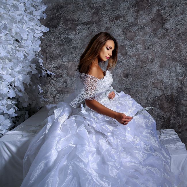 Side view of a bride in a white wedding dress sitting elegantly against a textured wall.