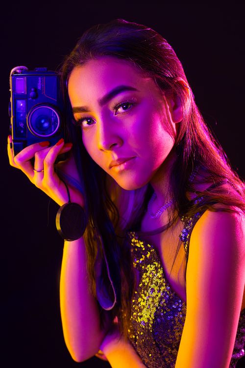 Free Elegant woman in a sequined dress holding a vintage camera under dramatic lighting. Stock Photo