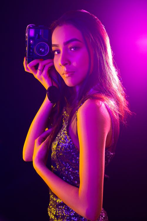 Free A stylish woman posing with a vintage camera under bright, colorful lighting. Stock Photo