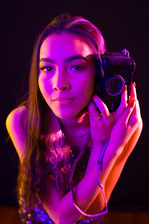 Free Artistic portrait featuring a woman holding a vintage camera in vibrant lighting. Stock Photo