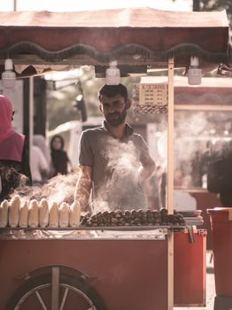 A street vendor selling roasted corn and chestnuts from a cart on a busy outdoor street.