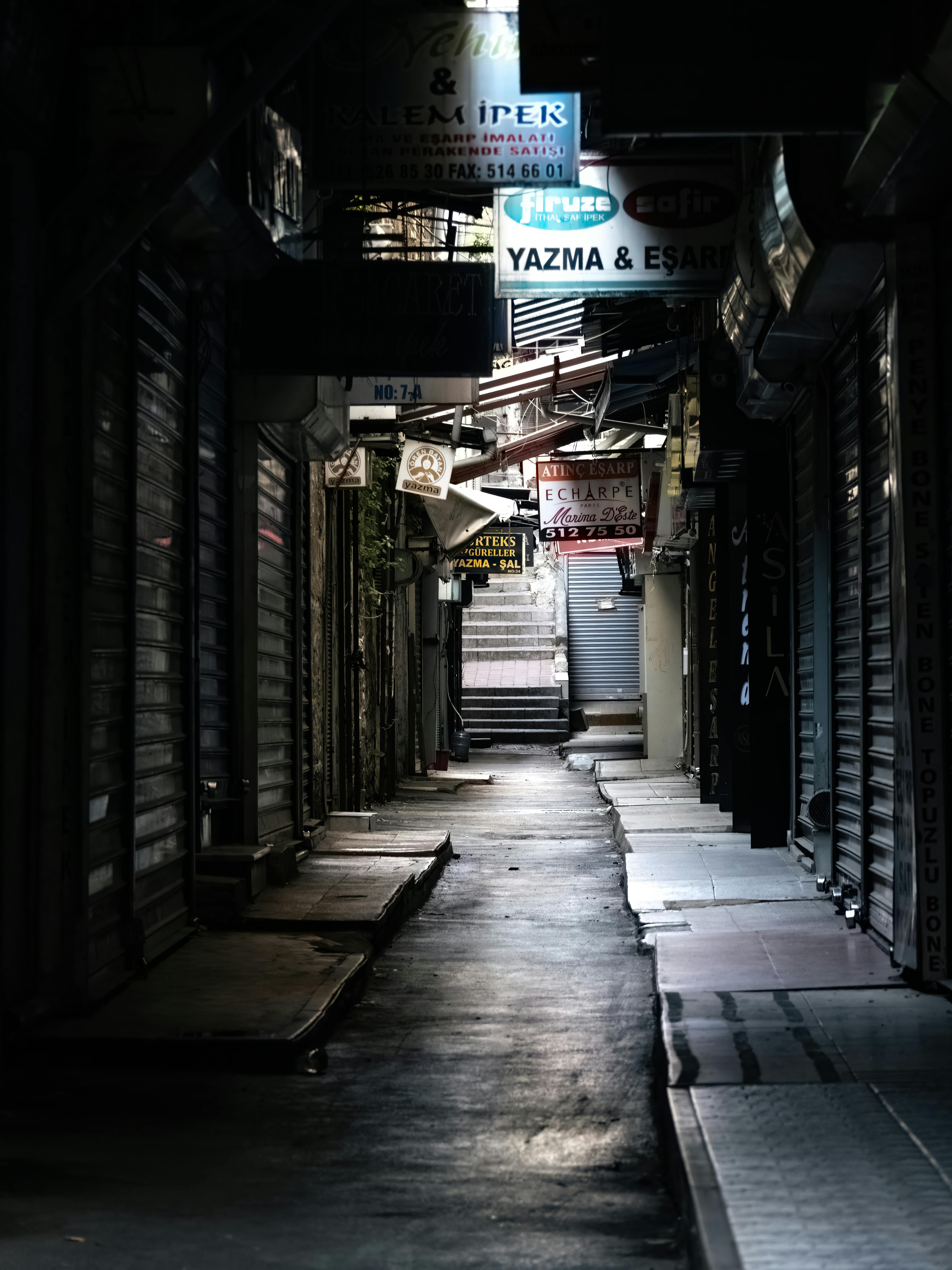 A narrow urban alleyway with closed shops and illuminated signs at night.